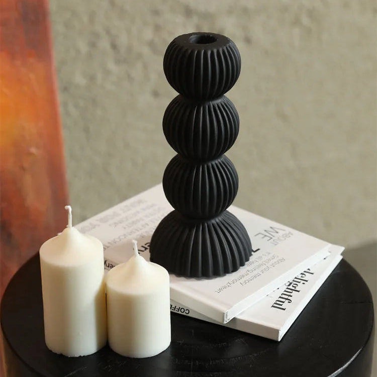Black textured candle holder with two white candles on a table.
