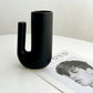 Black U-shaped vase on a white surface with a magazine underneath