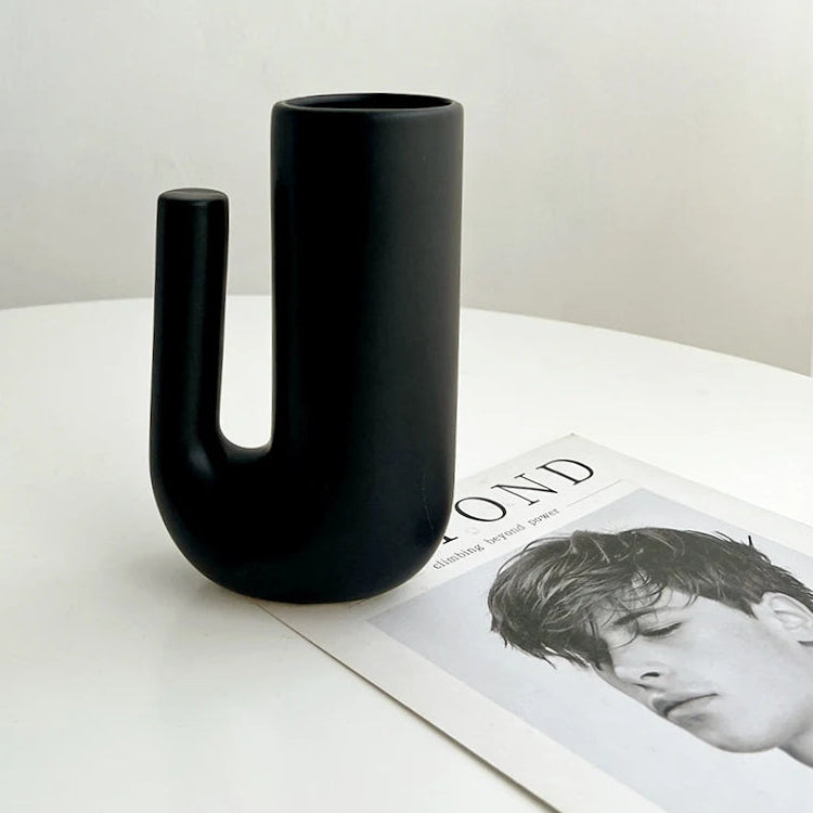 Black U-shaped vase on a white surface with a magazine underneath