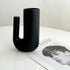 Black U-shaped vase on a white surface with a magazine underneath