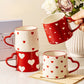 Set of red and white heart-patterned mugs on a surface with a decorative background.