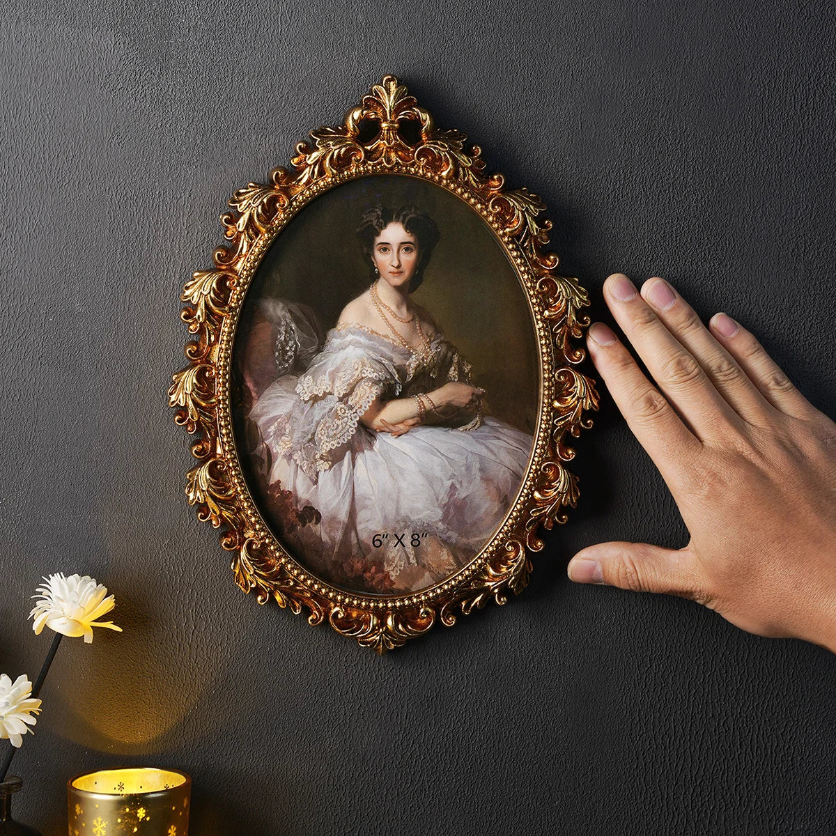 Decorative portrait of a woman in an ornate gold frame on a dark wall, with a hand reaching towards it.