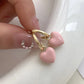 Pink heart-shaped earrings with gold hooks held by a hand against a white background