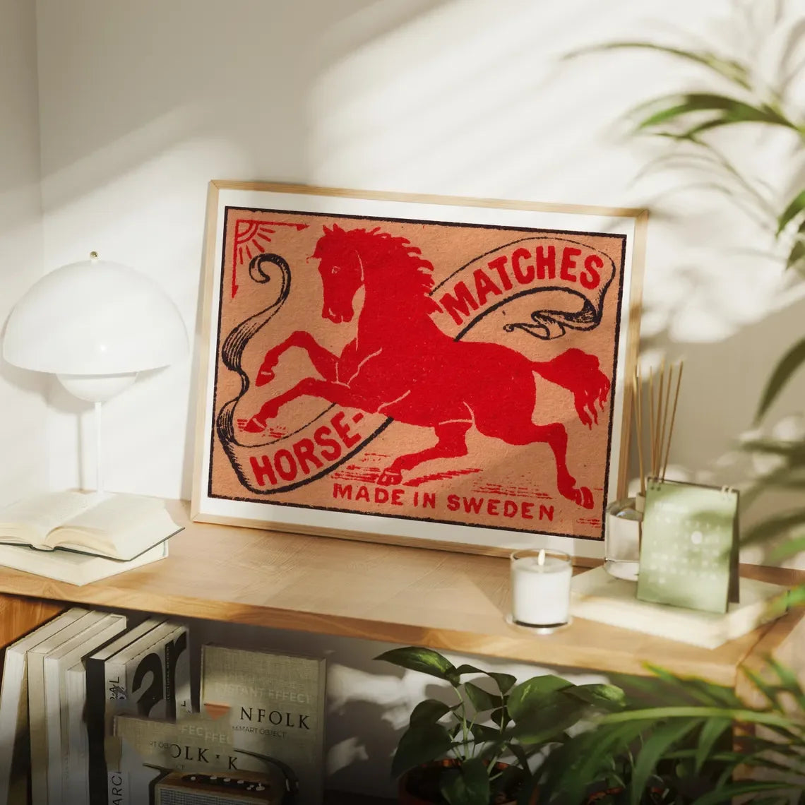 Framed vintage matchbox art with a horse design on a shelf.