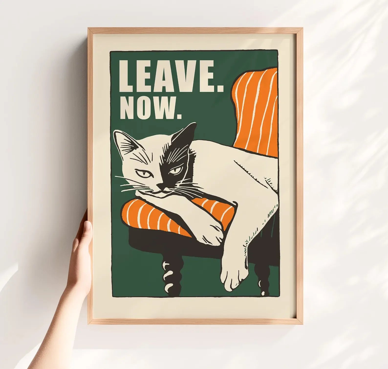 Framed poster with a cat illustration and text 'LEAVE. NOW.' on a white wall.