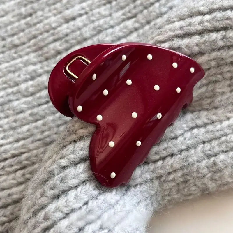 Red hair clip with white polka dots on a textured gray background