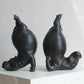 Two black ceramic sculptures of seals on a white surface with a light gray background