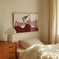 Room interior with a bed, wooden nightstand, and framed artwork on the wall.
