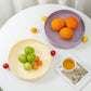 Fruit on two plates with a cup of tea and newspaper on a white table.