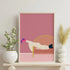 Framed abstract artwork of a reclining figure on a pink background, displayed on a shelf with decorative items.