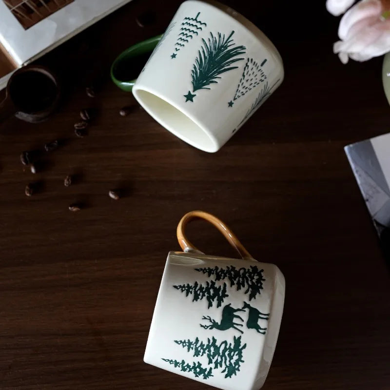 Two ceramic mugs with nature-themed designs on a wooden surface.