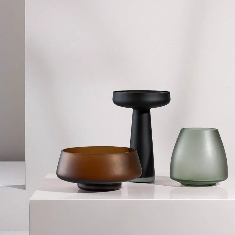 Three decorative vases in brown, black, and green on a white surface with a light gray background