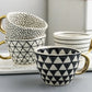 Set of patterned ceramic mugs with gold handles on a marble surface.