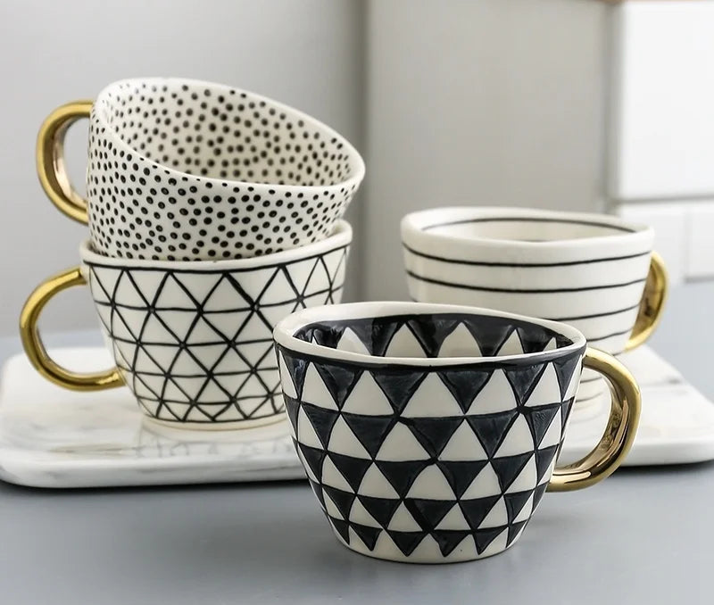 Set of patterned ceramic mugs with gold handles on a marble surface.