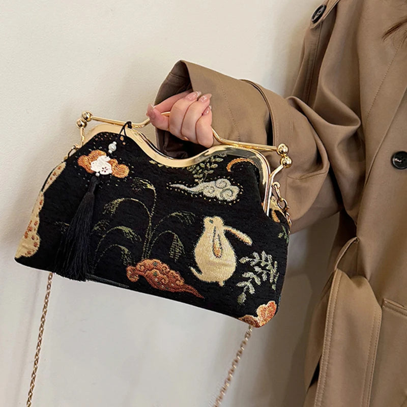 Person holding a black embroidered handbag with floral and animal designs.