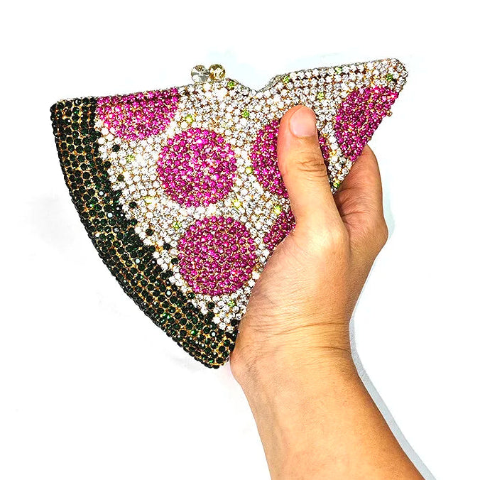 Hand holding a pizza-shaped clutch bag with gemstone embellishments on a white background