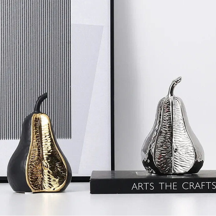 Decorative pear sculptures in black and gold, and silver and black, on a white surface with a modern interior background.