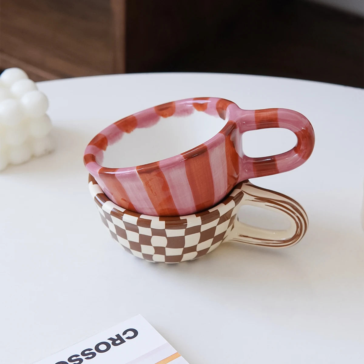 Two ceramic cups stacked on a white surface with a blurred background