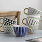 Set of patterned mugs with gold handles on a light surface.