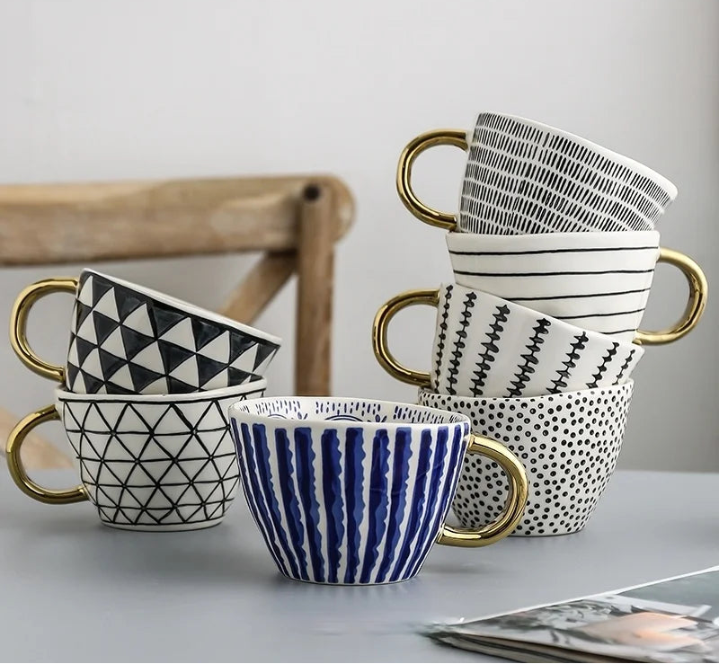 Set of patterned mugs with gold handles on a light surface.