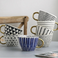 Set of patterned mugs with gold handles on a light surface.