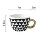 Ceramic mug with black and white triangle pattern and gold handle, shown with measurements on a white background.
