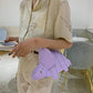 Person holding a light purple handbag with gold accents in an indoor setting.