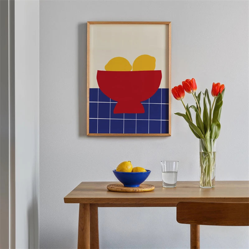 Modern interior with a framed abstract art piece, table with fruit and glass, and vase with flowers.
