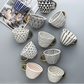 Collection of ceramic cups with various geometric patterns on a gray surface.