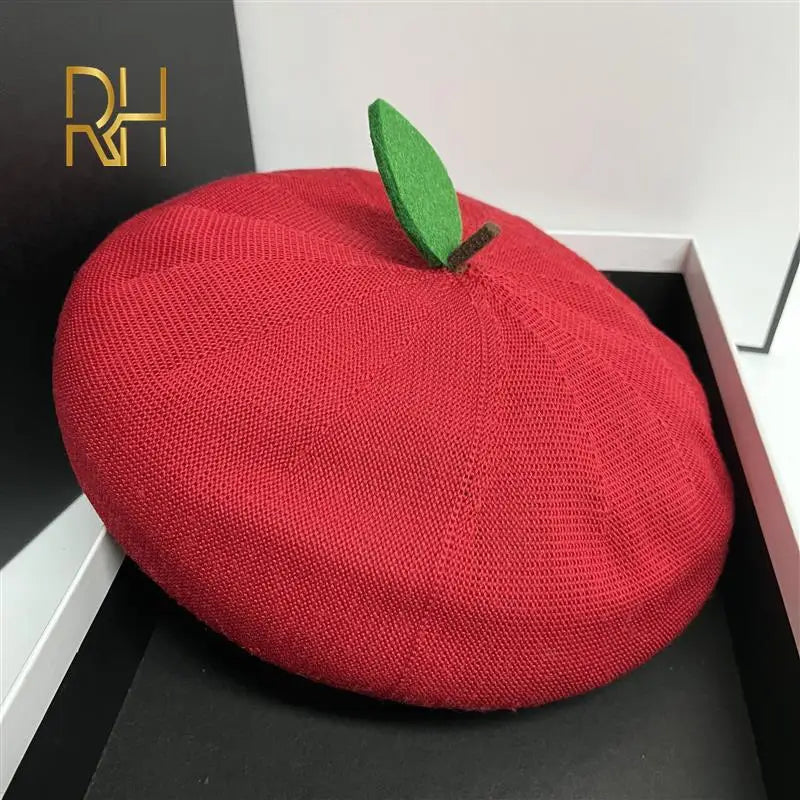 Red beret with a green leaf on a black surface, with a brand logo in the corner.