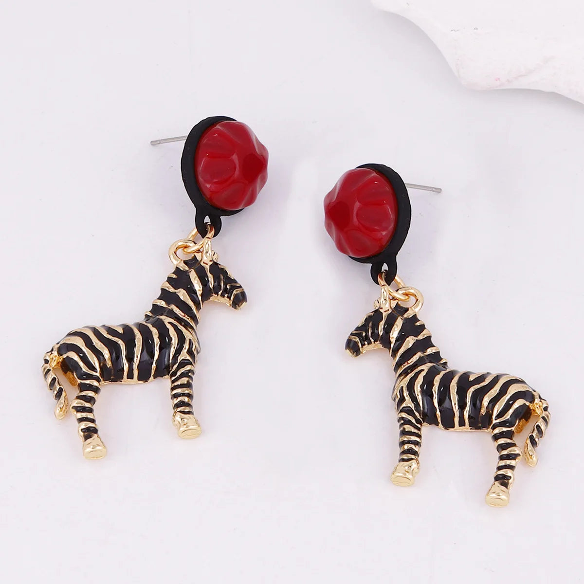 Zebra-shaped earrings with red flower-like pendants on a white background
