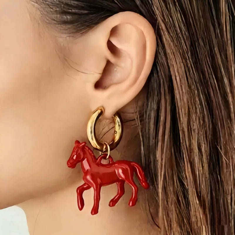 Red horse-shaped earring on a gold hoop worn by a person with brown hair.