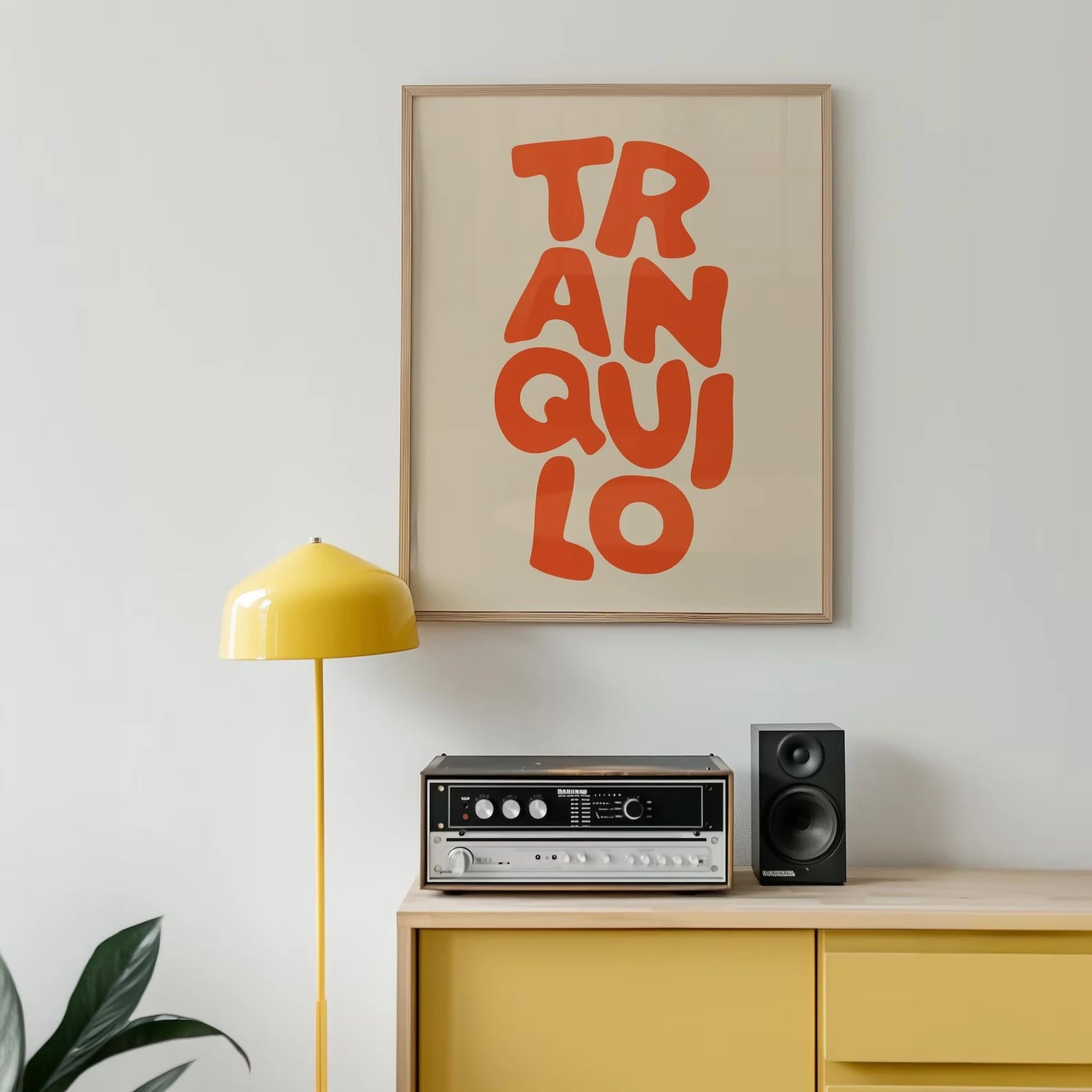 Framed artwork with 'TRANQUILO' on a wall above a yellow cabinet with audio equipment.
