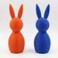 Orange and blue rabbit-shaped vases on a textured surface with a neutral background
