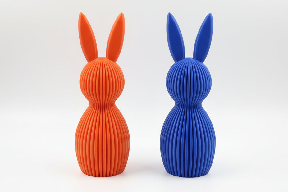 Orange and blue rabbit-shaped vases on a textured surface with a neutral background