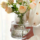 Clear textured vase with flowers held by a person wearing a white sweater.