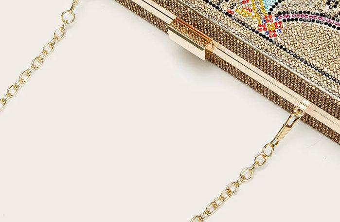 Gold chain attached to a decorative clutch bag on a white background
