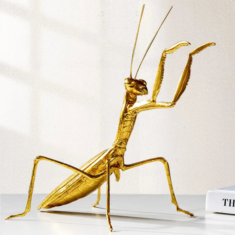 Gold praying mantis sculpture on a white surface with a light background