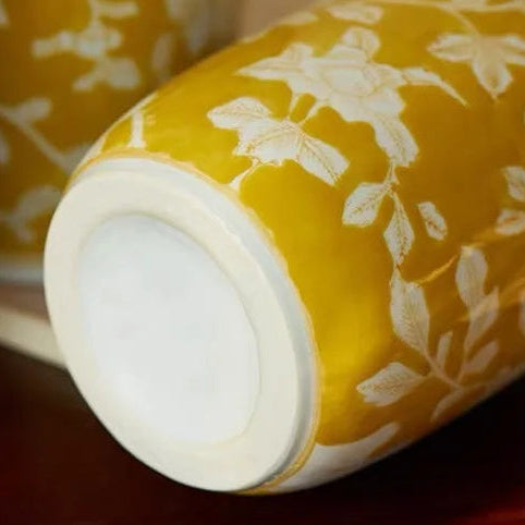 Yellow ceramic vase with white floral patterns on a wooden surface