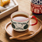 Ceramic mug with red handle on a wooden tray with a wooden spoon, on a wooden surface.