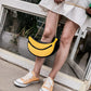 Person wearing a banana-shaped handbag and orange sneakers on a sidewalk.