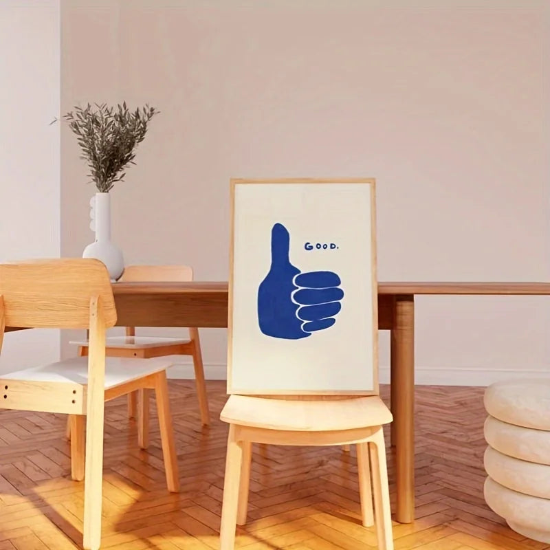 Dining room with wooden table and chairs, featuring a framed print with a blue hand gesture and 'Good' text.