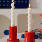 Two spiral candles in red holders on a white surface with a colorful background.