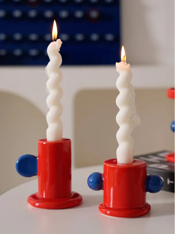 Two spiral candles in red holders on a white surface with a colorful background.