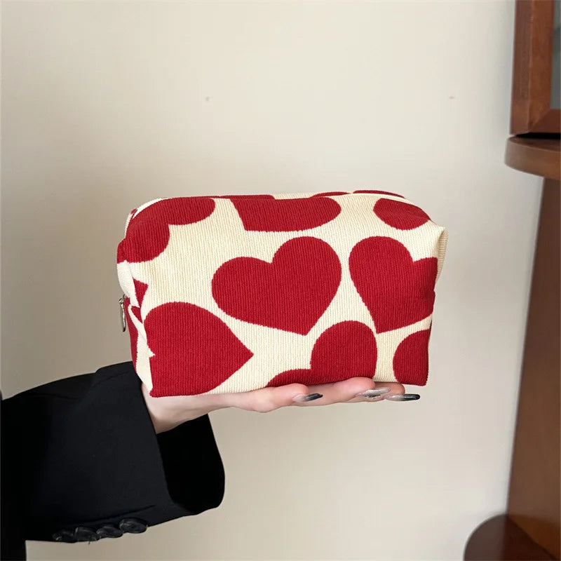 Red heart-patterned pouch held by a person against a neutral background
