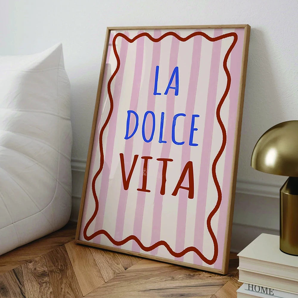 Framed artwork with 'LA DOLCE VITA' text on a striped background in a home setting.