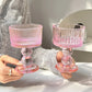 Person holding two pink glass candle holders on a white surface