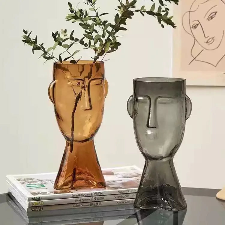 Two glass face vases, one brown and one gray, on a surface with a light background.