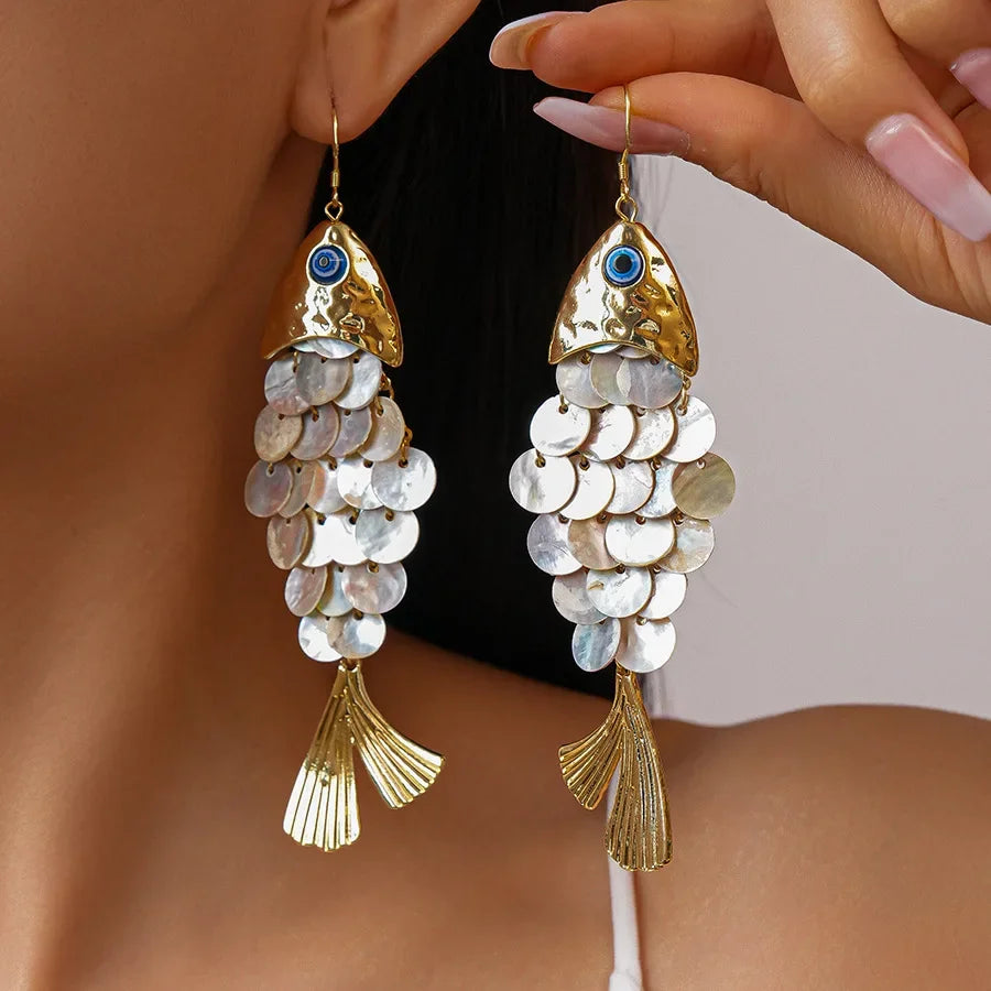 Gold fish-shaped earrings with circular components worn by a person.