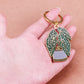 Hand holding a keychain with a plant design against a beige background